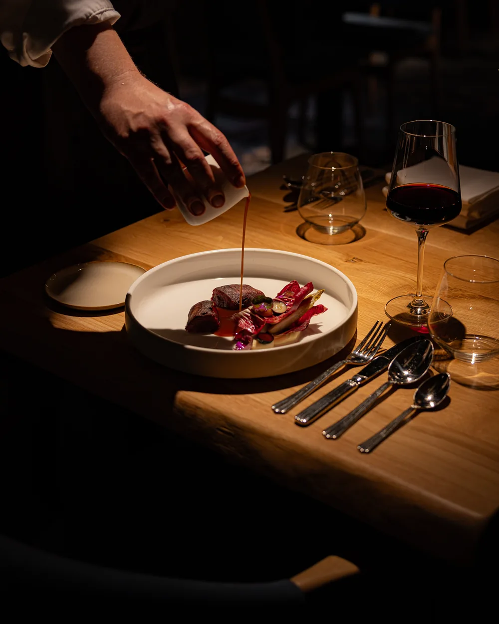 Saus wordt aan tafel over een gerecht geschonken, met rode wijn ernaast