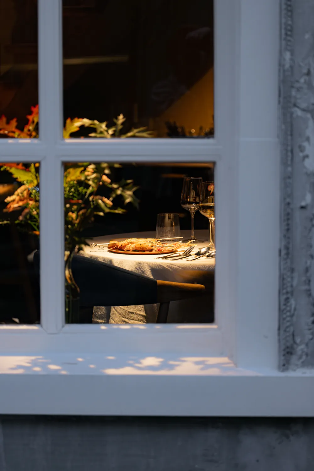 Een gedekte tafel in het avondlicht, gezien door het raam