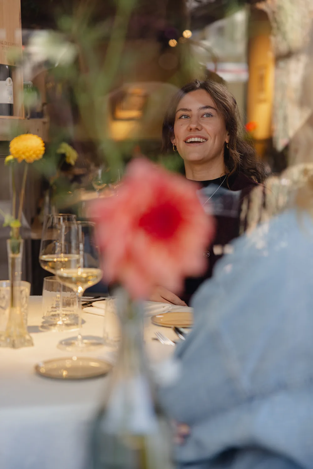 Een lachende gast aan tafel, met een bloem op de voorgrond